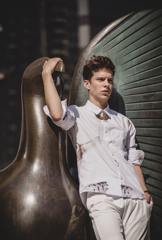 Menswear on location, model leaning against a large bronze sculpture in sunlight