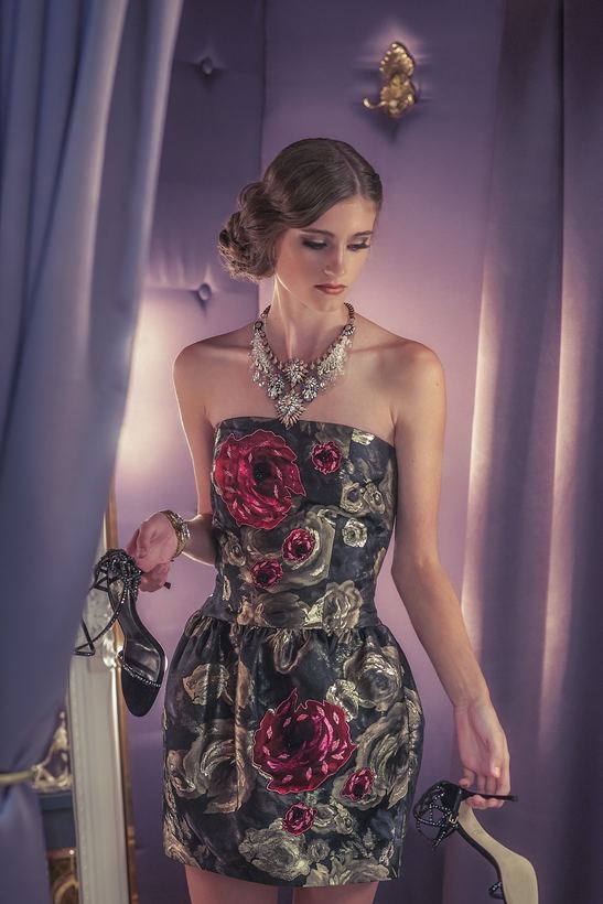 Evening editorial — model in a rose-brocade strapless dress carrying her heels