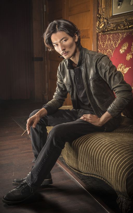 Menswear editorial — model in a worn leather jacket seated in a wood-panelled salon