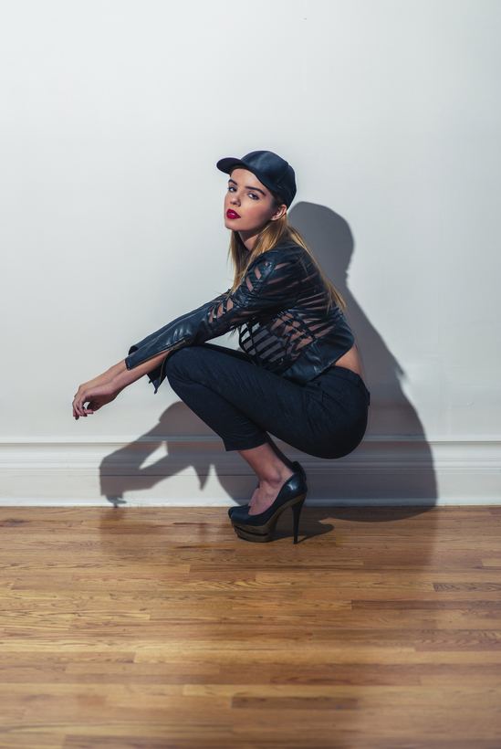 Studio fashion portrait, model crouched against a white wall casting a hard shadow